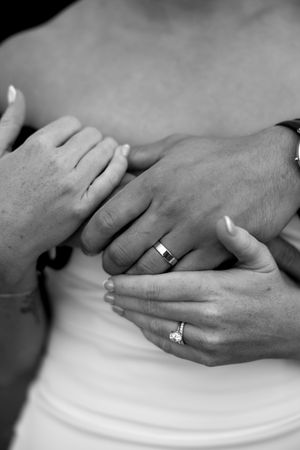 Close-up black and white photo of hands with wedding and engagement rings against a white garment.