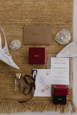 Wedding accessories and jewelry laid out on textured burlap including Cartier boxes and white invitation cards.