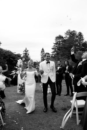 Wedding party celebrating and dancing on a grassy lawn with trees in the background.