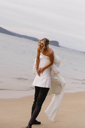 Couple embracing on a sandy beach with ocean and cloudy sky in the background.