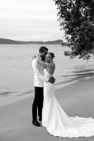 Black and white beach wedding photography with couple embracing on sandy shoreline.