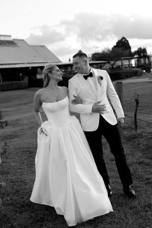 Black and white photo of a bride in strapless gown and groom in white tuxedo walking together on their wedding day.