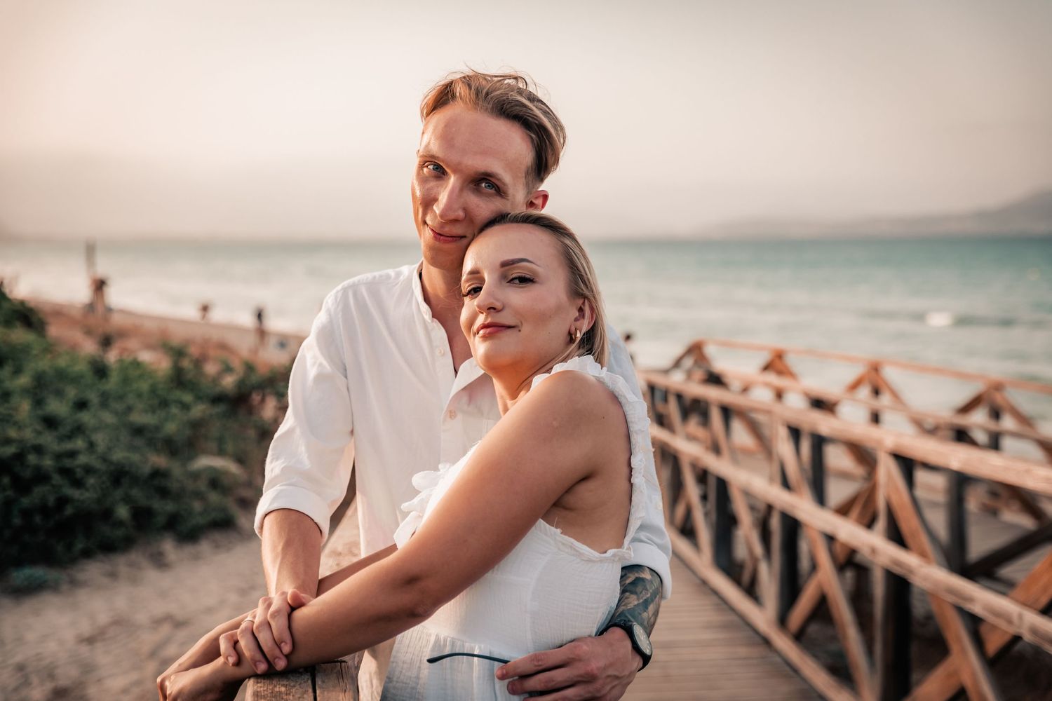 Portrait of a man and a woman both dressed in white and looking into the camera with blurred ocean in background.