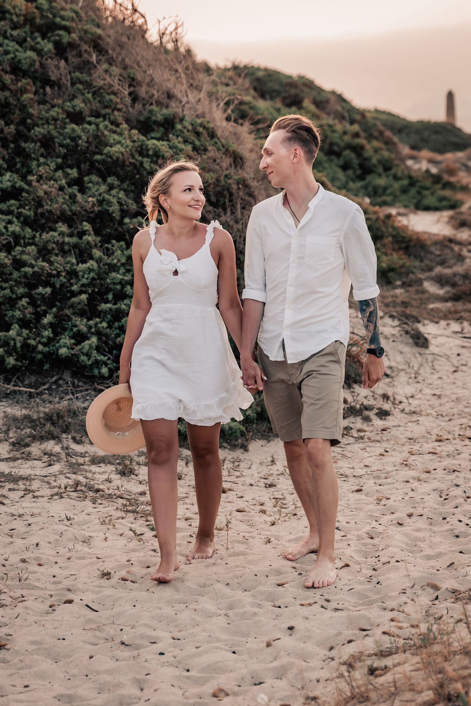 Couple holding hands and walking along the water's edge at golden hour.