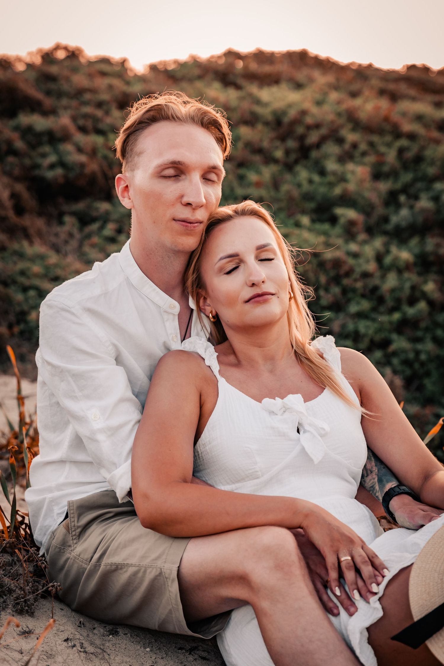 Close-up of a couple's emotional embrace, eyes closed, on the beach at sunset.