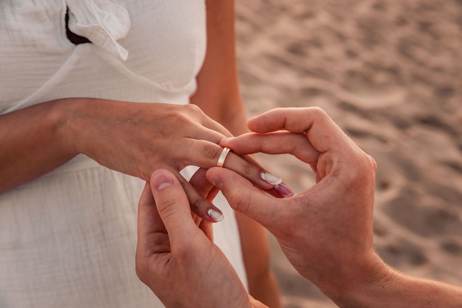 Detail shot of an engagement ring being placed on a hand with a blurred background.