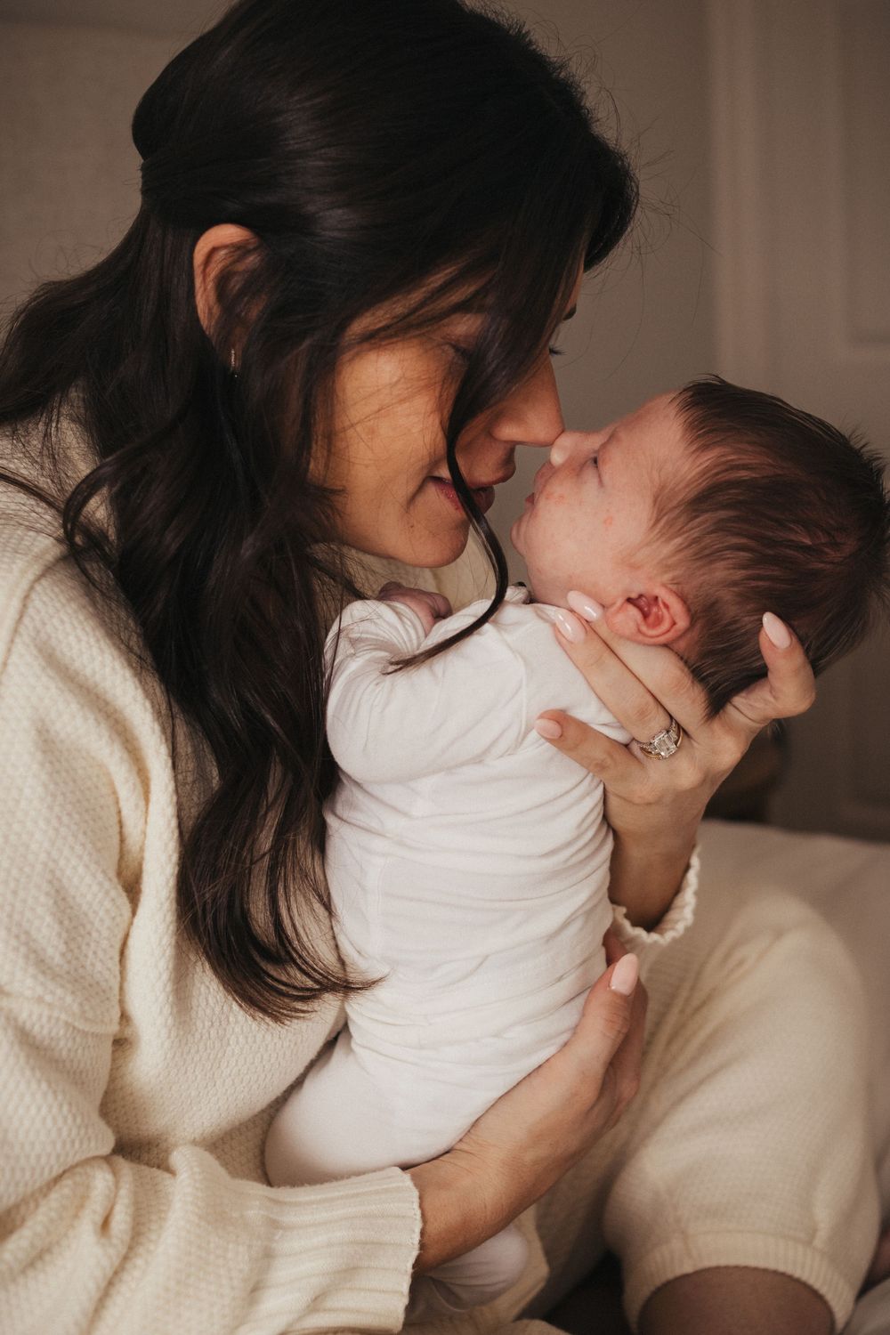 Intimate moment between parent and baby in white outfit against cream background.