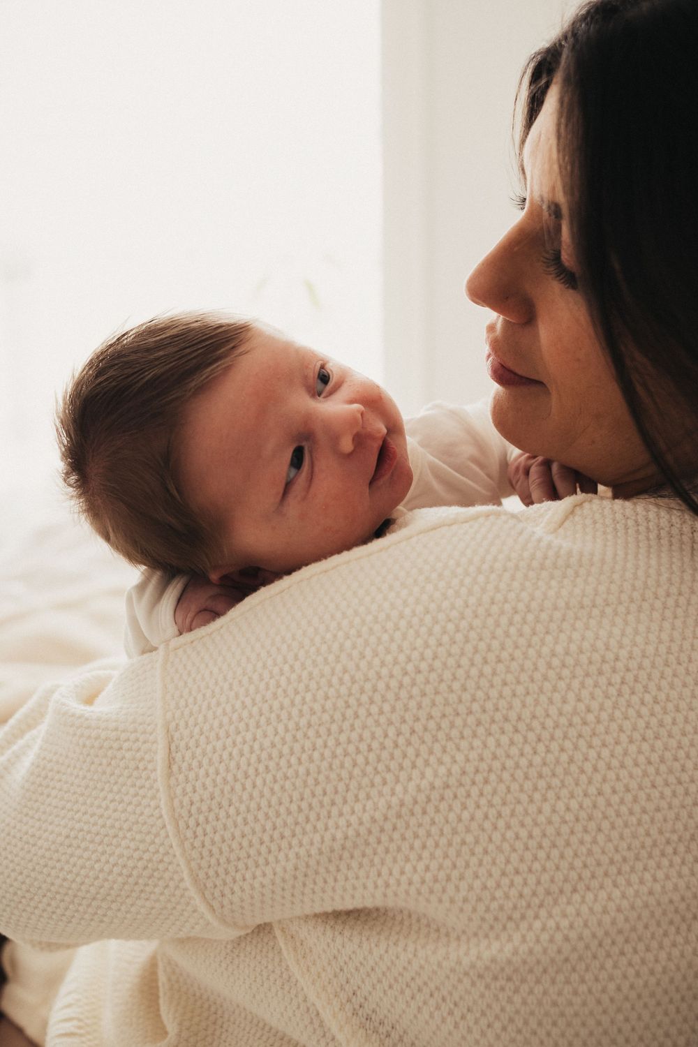 Sweet candid moment between parent and smiling baby against light background.