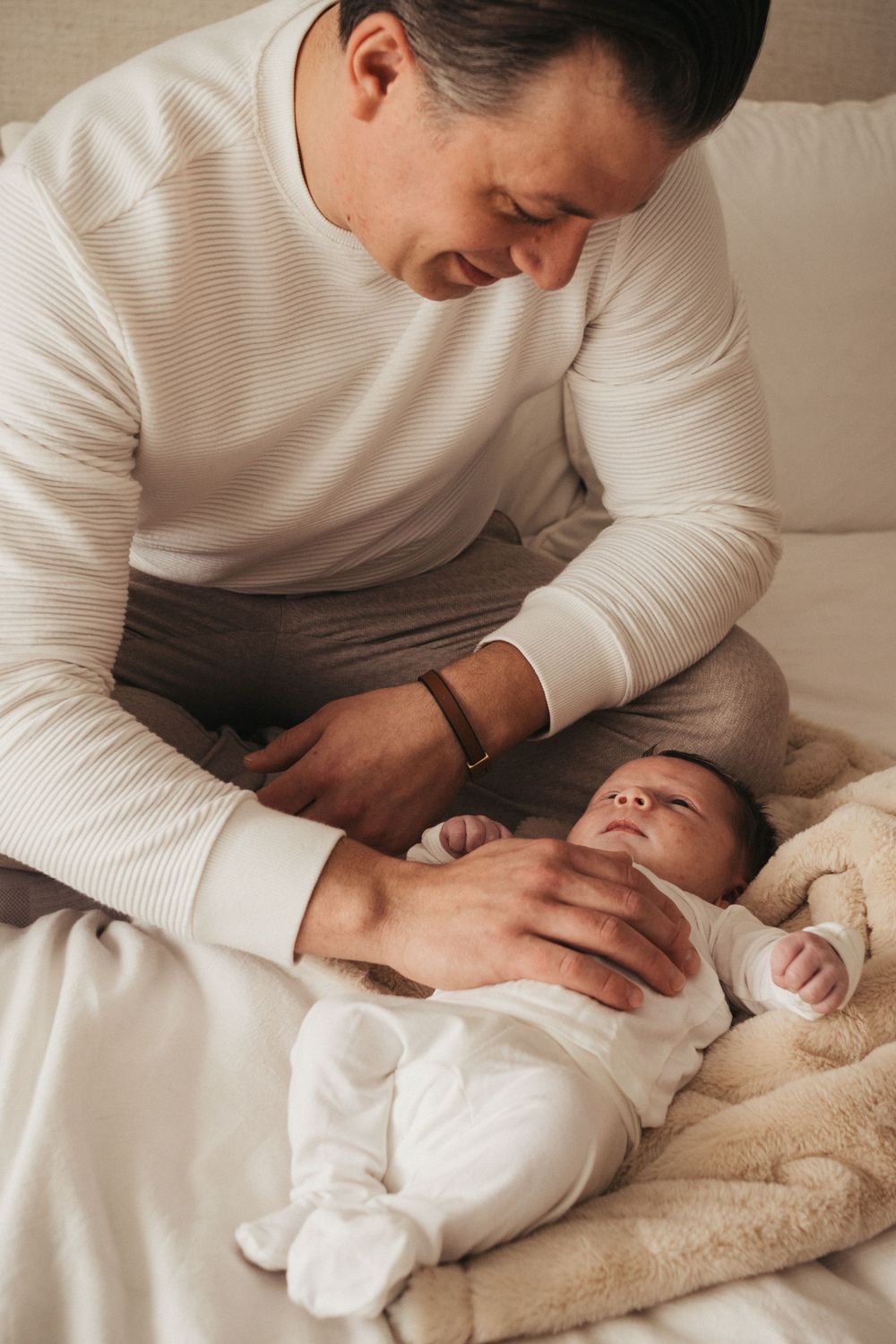 Parent in white sweater tenderly caring for baby lying on cream blanket.