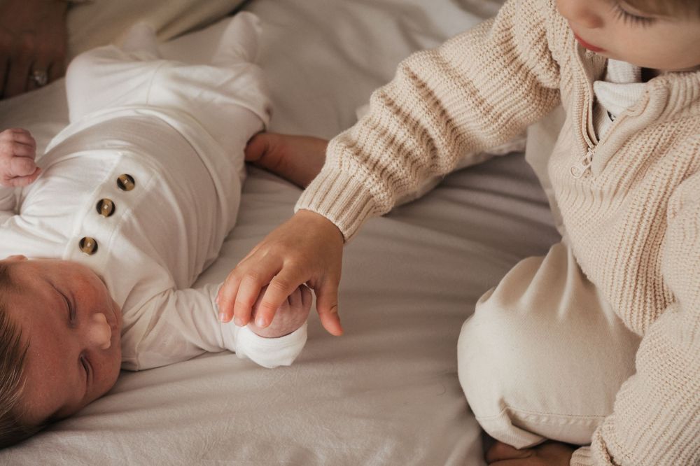 Close-up of tiny baby in white outfit being gently touched on cream bedding.