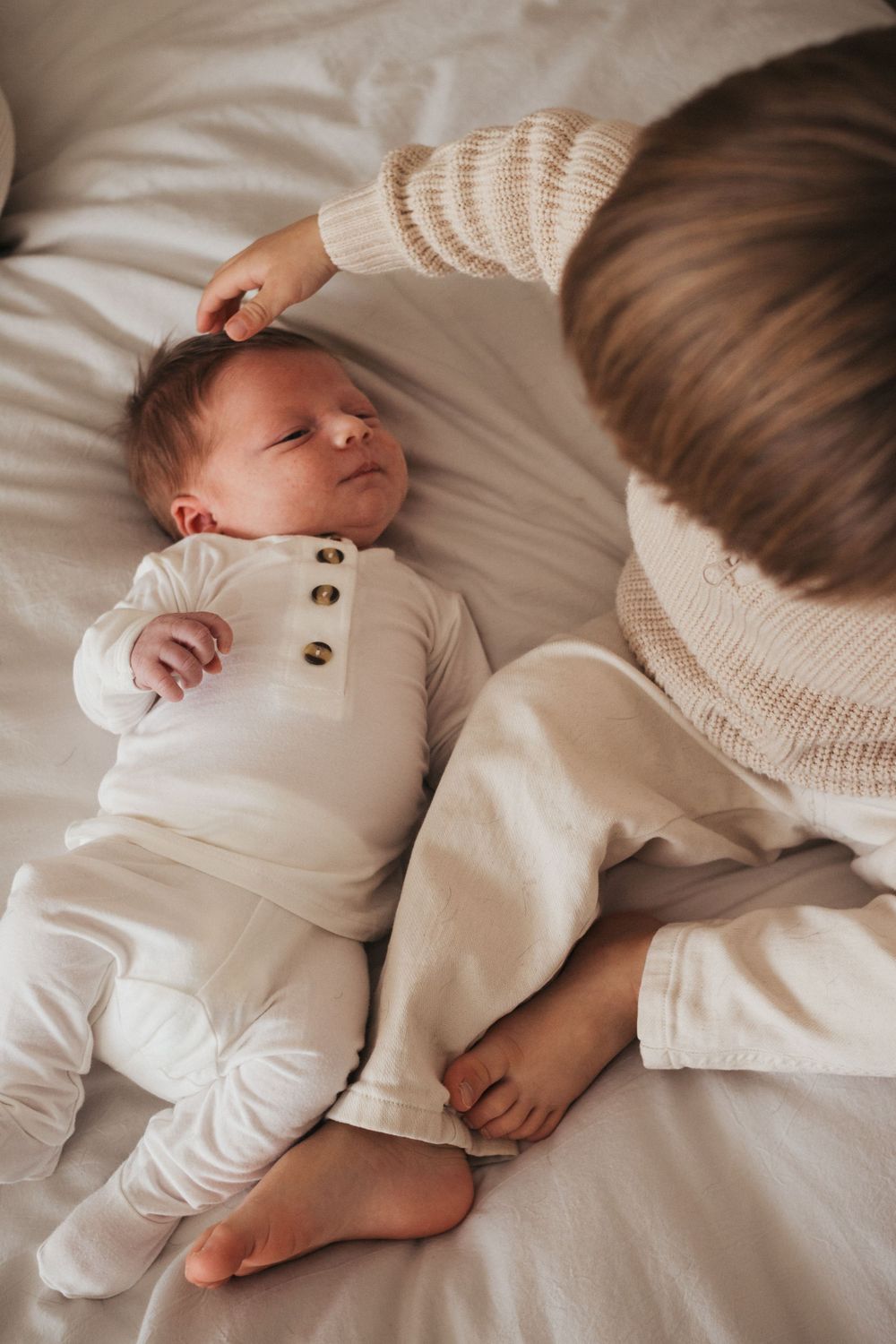 A tender moment with a newborn baby resting peacefully in white clothing on soft bedding.