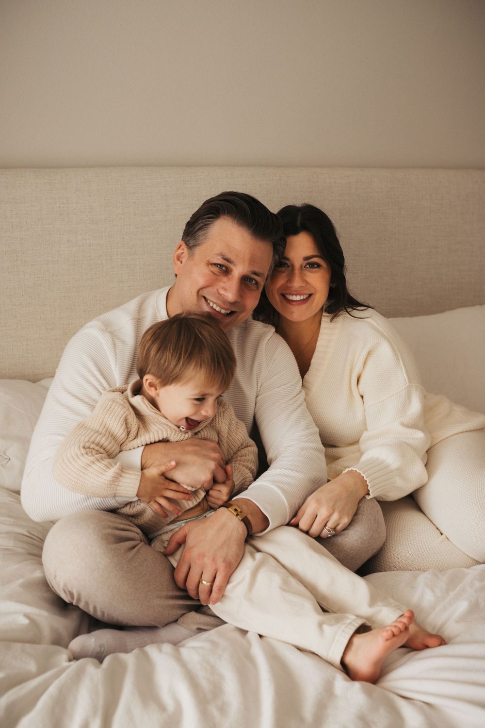 A cozy family moment on the bed wearing neutral cream and white outfits.