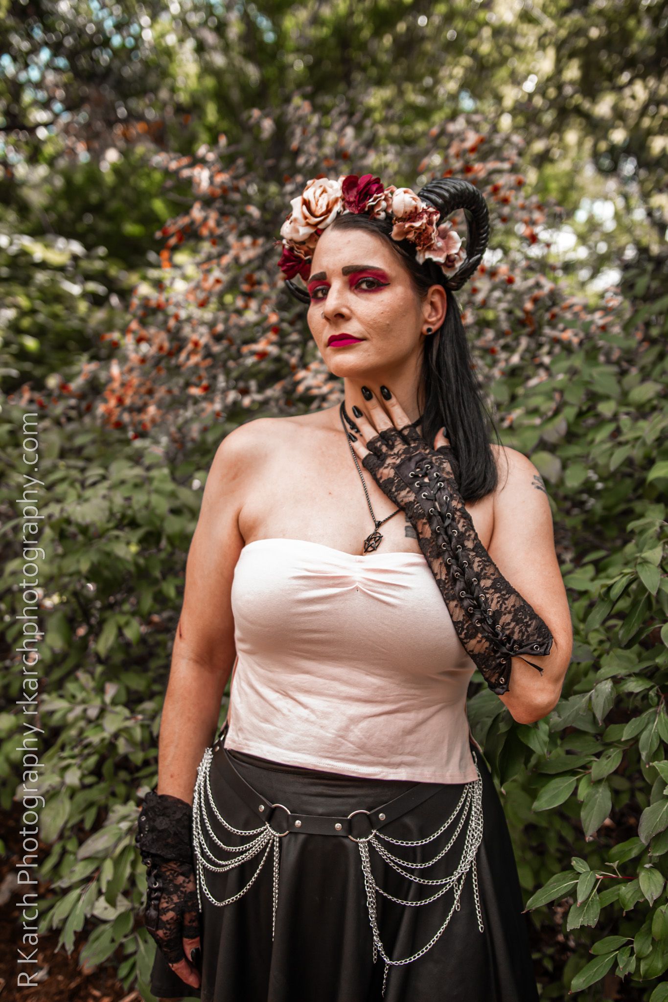 A gothic-styled model poses in floral crown and lace gloves against a natural garden backdrop.