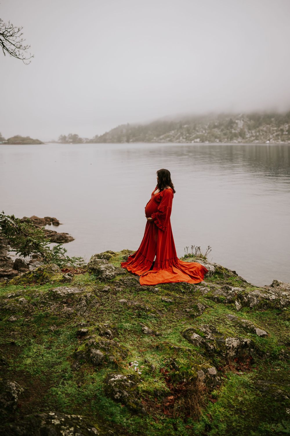 Scenic maternity photo of woman red dress holding bump on ledge over looking at ocean Neck Point Nanaimo Vancouver Island