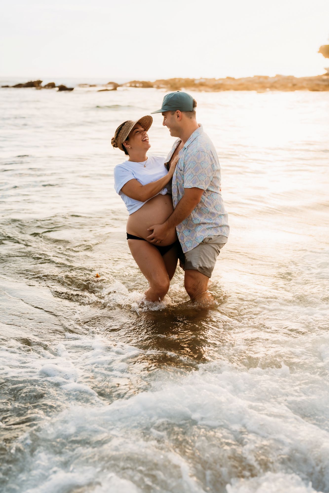 A couple embraces while standing in ocean waves at sunset creating a romantic beach scene.
