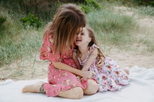 Two people sharing a joyful moment on white blanket outdoors.