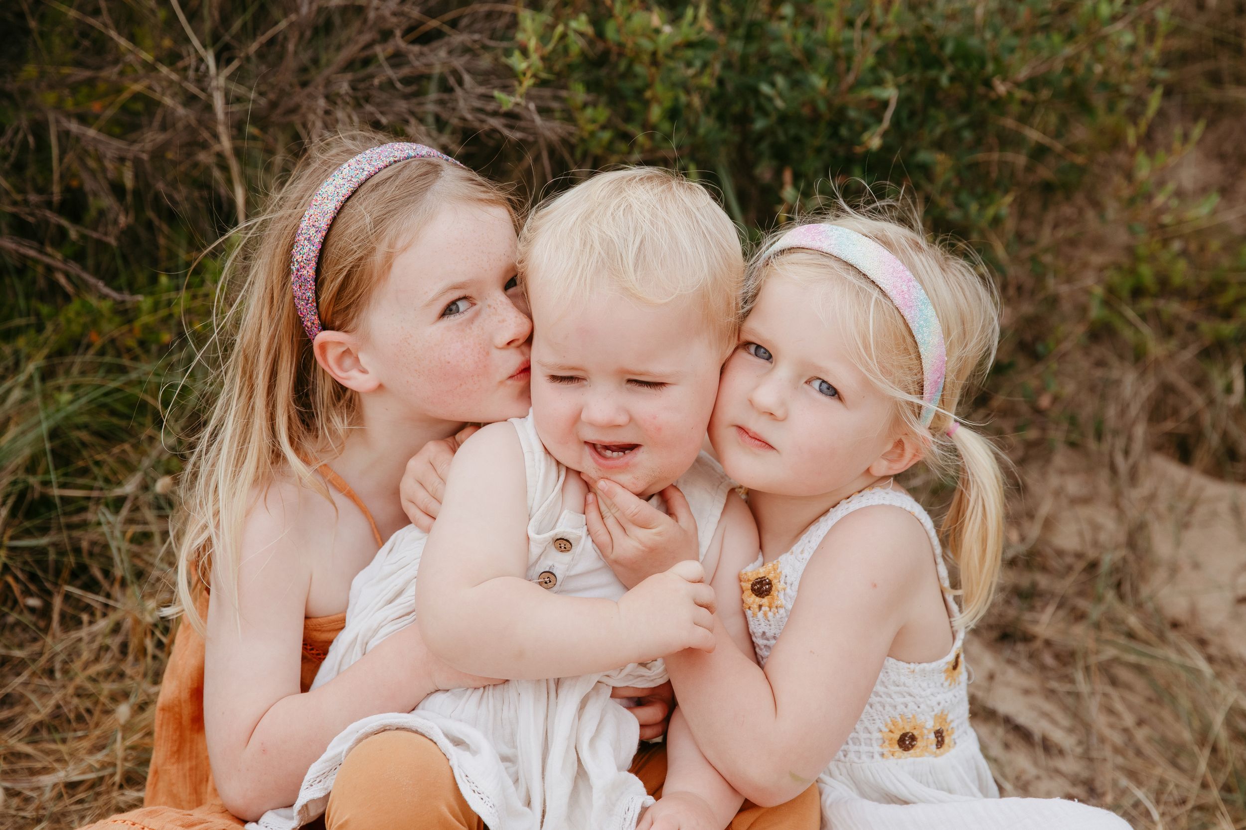 Three young children sharing a sweet moment together outdoors.