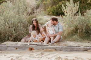 Family sitting together on sandy ground surrounded by green foliage.