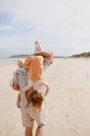Parent holding children playfully upside down on sunny beach.