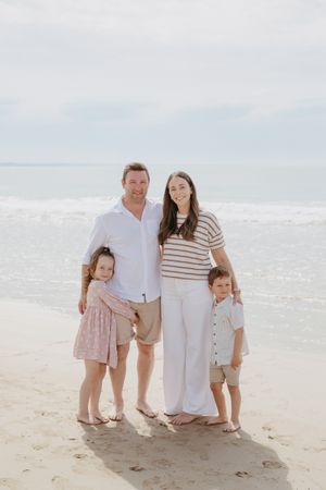 A family dressed in coordinated beachwear poses together on a sunny beach.