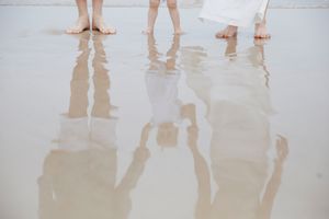 Reflections of family members' feet in wet sand on a beach.