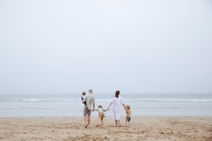 A family walking hand in hand towards the ocean on a misty beach.