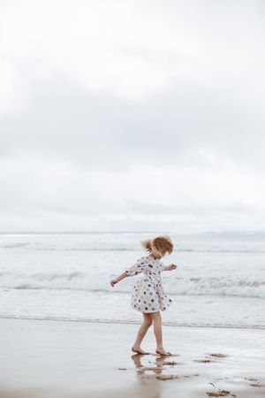 Person in polka dot dress twirling on beach near ocean waves.
