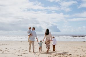 A family holding hands while walking along a scenic beach under blue cloudy skies.