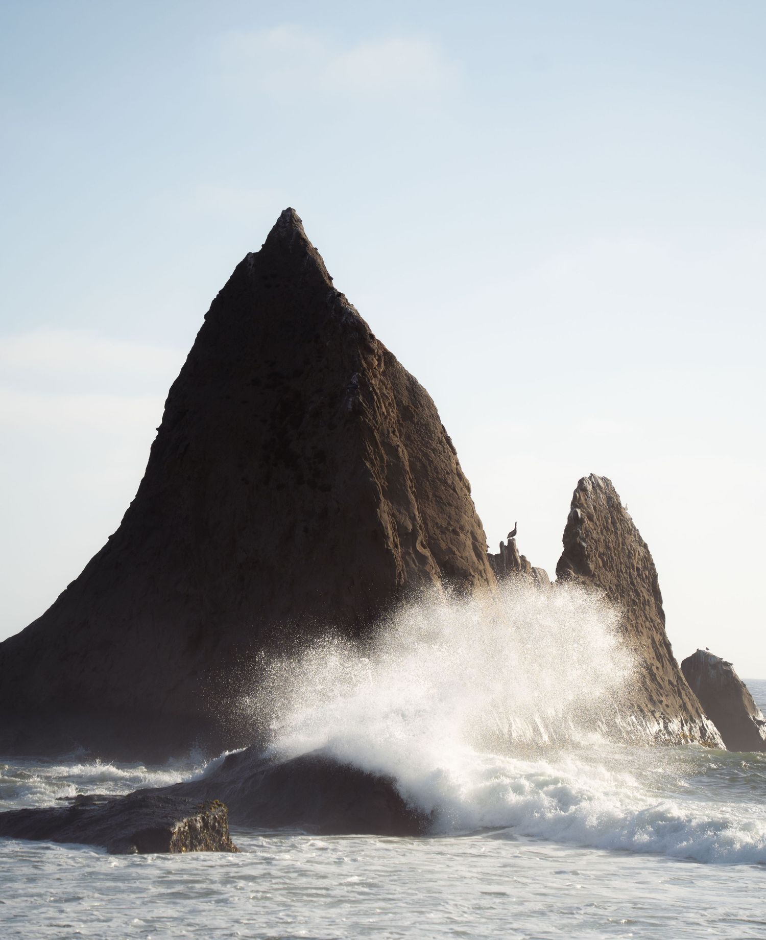 Dramatic coastal rock formation with crashing waves against misty sky.