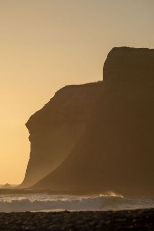Dramatic silhouettes of coastal cliffs against a golden sunset sky.