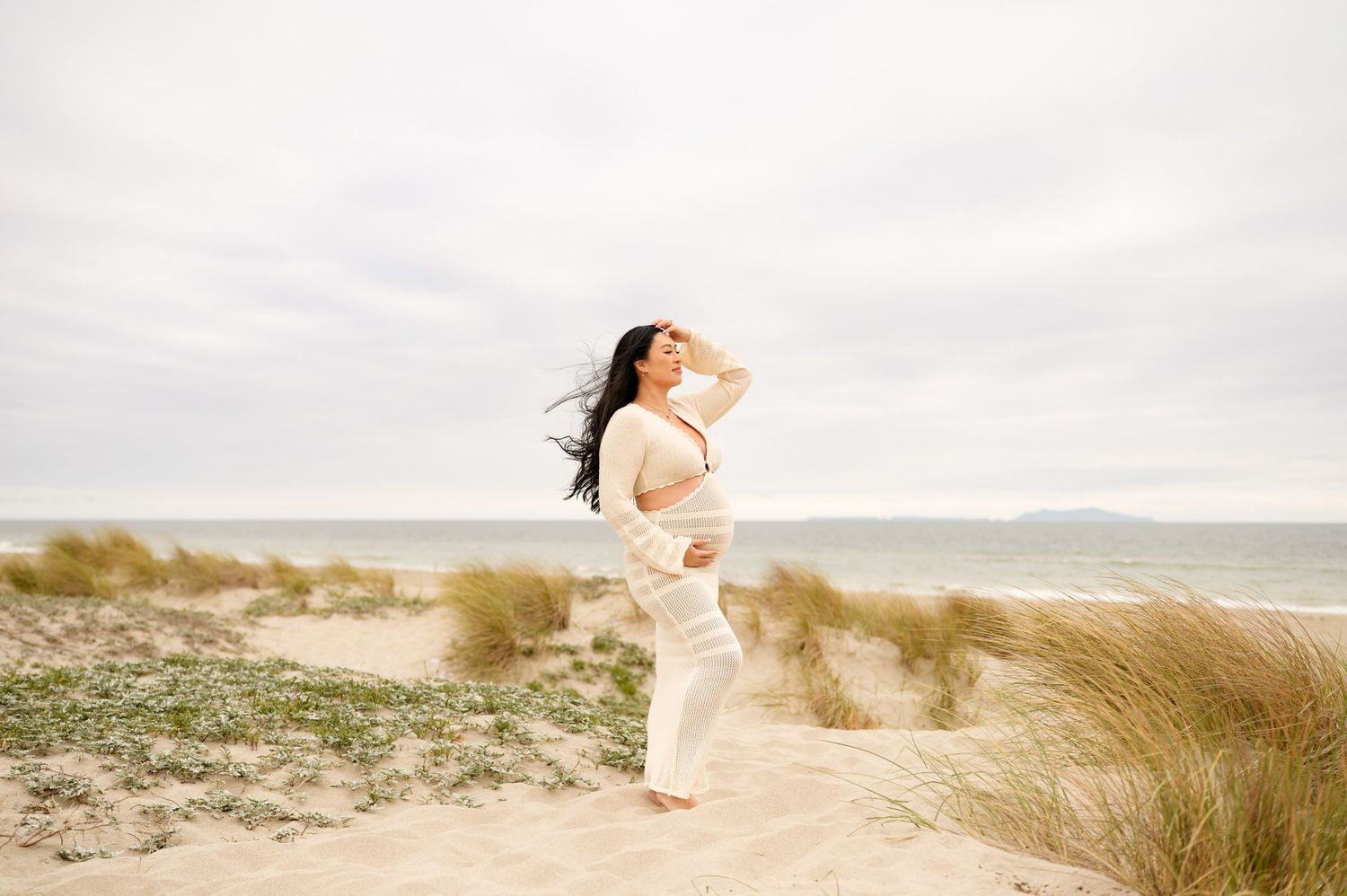 Ventura beach maternity photoshoot of woman posed in crochet dress on beach sand dunes during her Santa Barbara babymoon