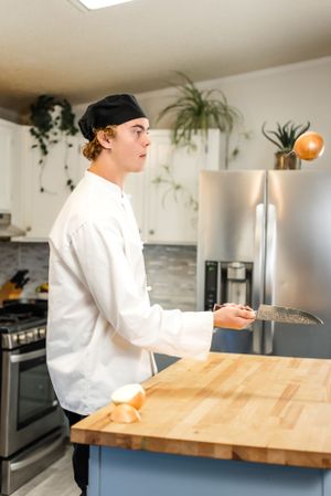 Chef in white uniform and cap preparing food at wooden kitchen counter.