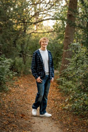 Person in plaid flannel and jeans standing on wooded trail during autumn.