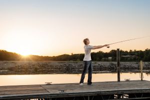 Person fishing from wooden dock at sunset.