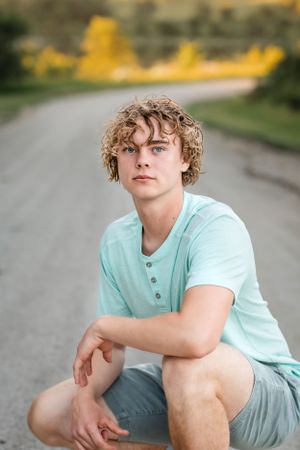 Person in mint henley shirt sitting outdoors on rural road.
