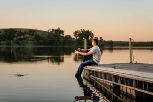 Person casting fishing line on wooden dock during golden hour.