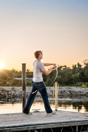 Person fishing on wooden pier at sunset over calm lake.