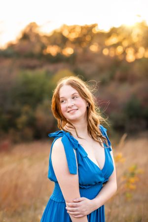 A woman in a blue dress poses at sunset with golden light creating a warm glow in the background.