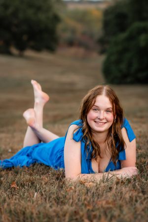 Woman in a bright blue dress lies on grass during an outdoor photo session.
