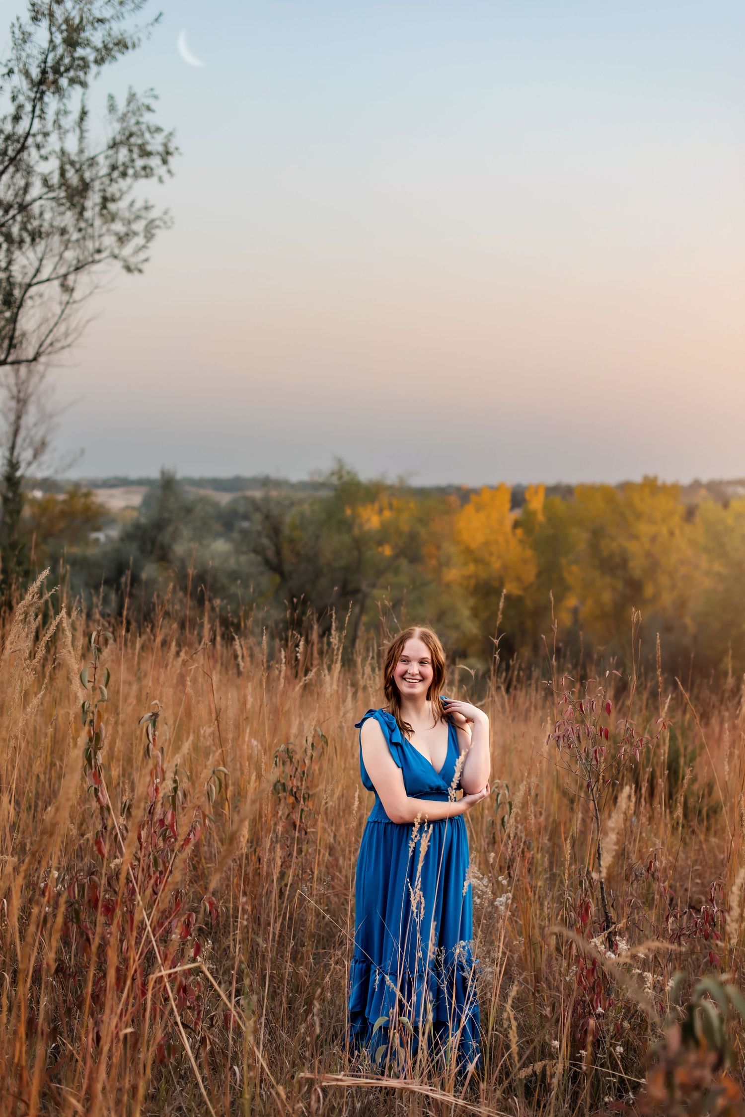 Woman in blue dress standing in tall autumn grass during sunset.
