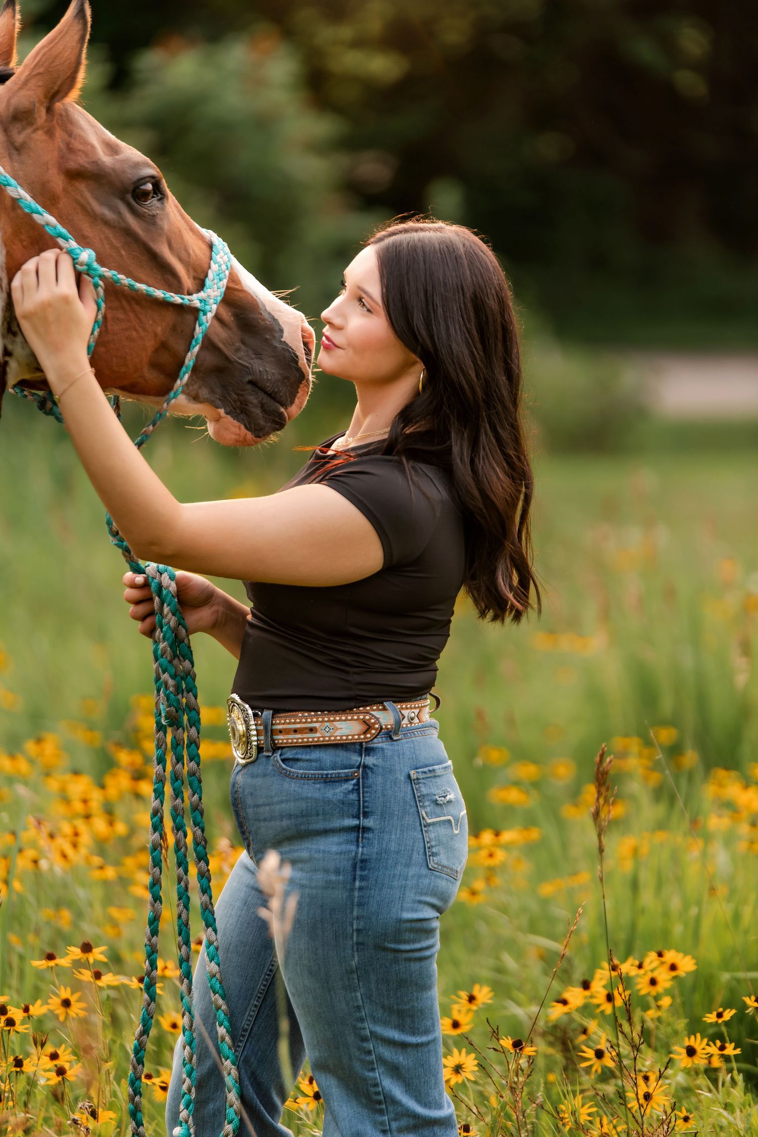 A chestnut horse and senior grad share a tender moment in a field of vibrant yellow wildflowers.