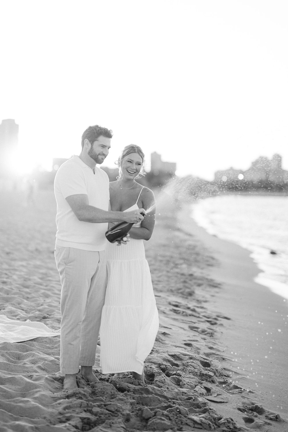 A couple in white attire shares a romantic moment on the beach shore during a misty day. - North Avenue Beach Chicago Engagement