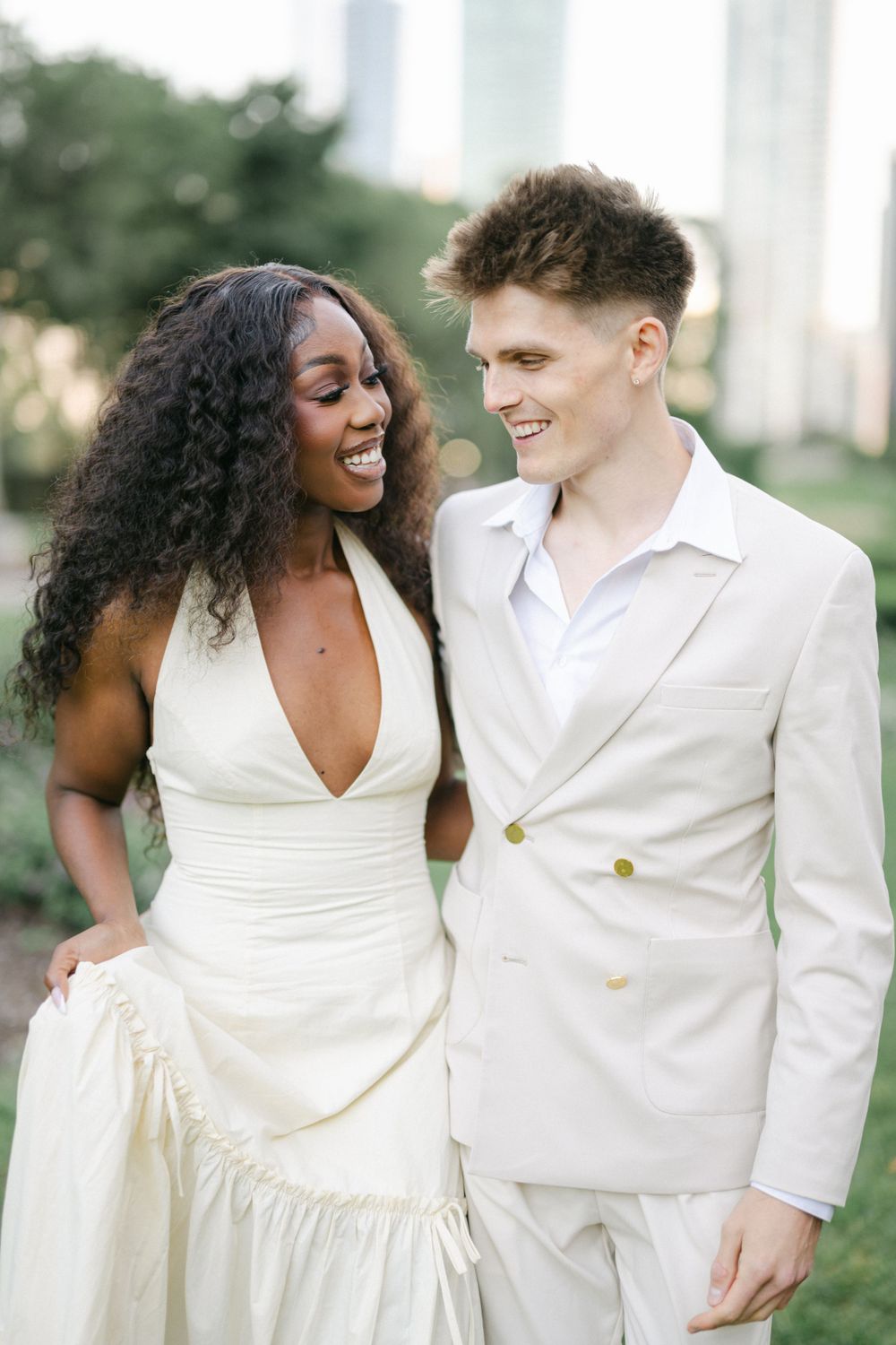 Happy couple wearing white formal attire laughing together outdoors with city buildings in background. - Grant Park Chicago