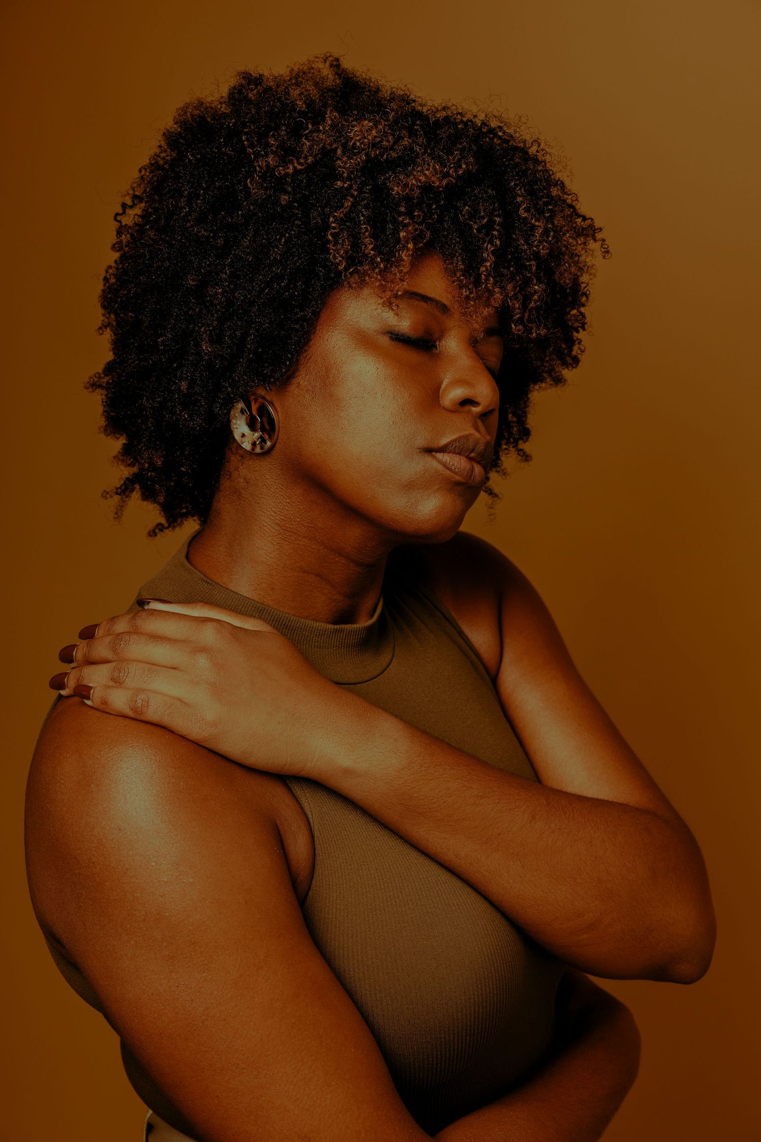 Artistic portrait with natural curly hair against warm brown background.