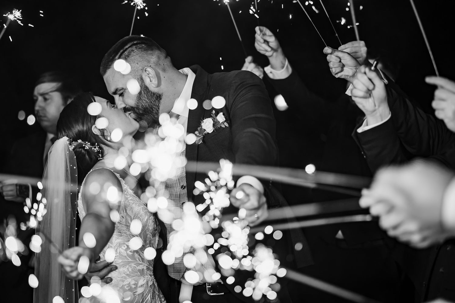 Black and white photo of a crowd holding sparklers creating glowing light trails during a nighttime celebration.