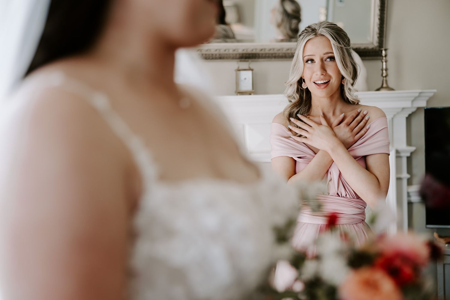 An emotional moment between a bride in a white gown and a person in pink during wedding preparations.