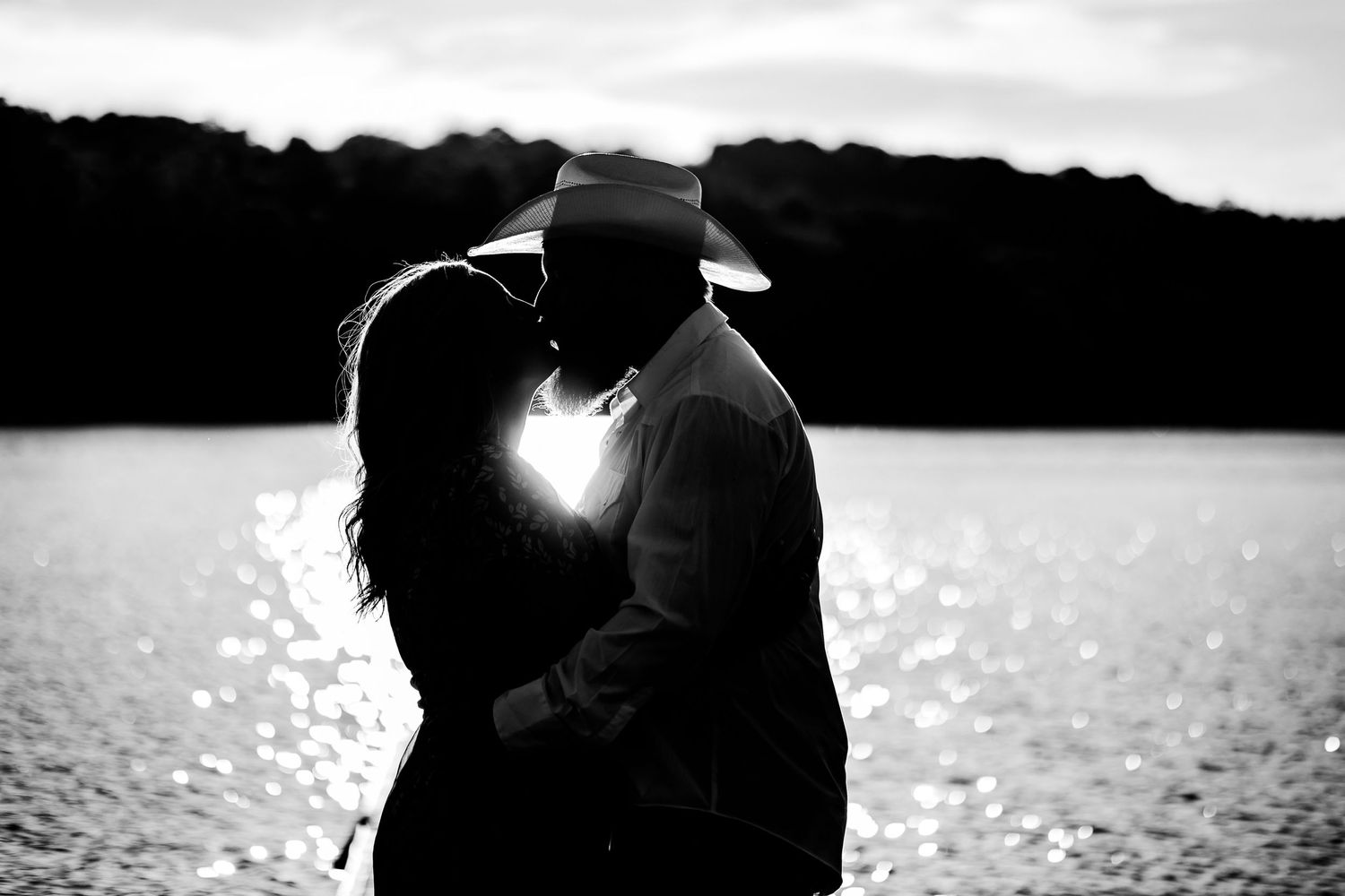 Romantic silhouette of couple embracing by a lake at sunset.
