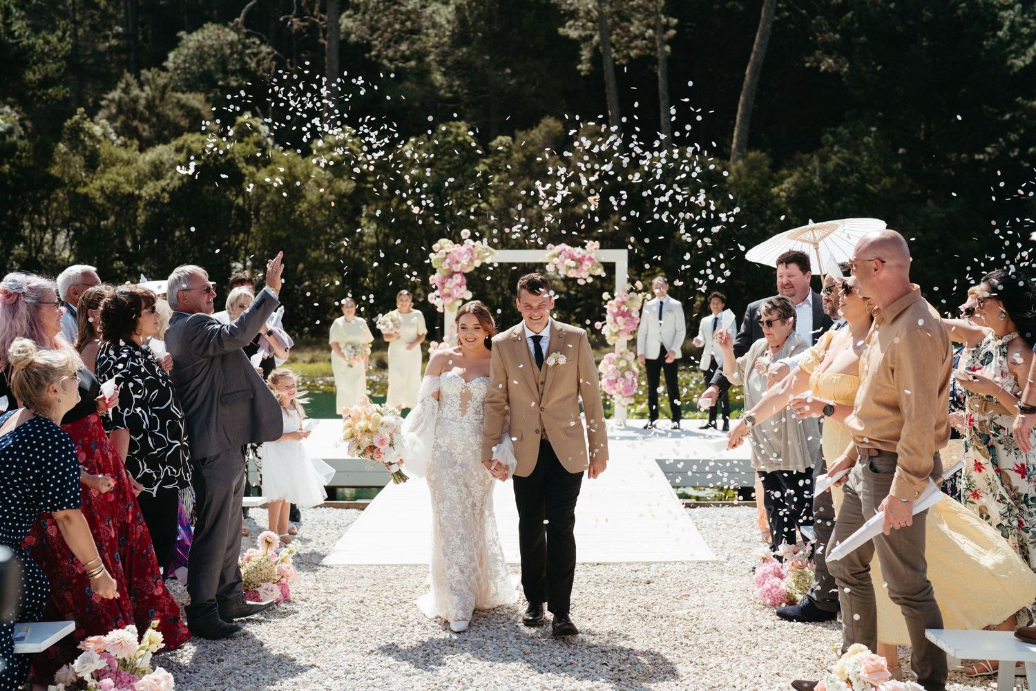 Wedding guests shower the newlyweds with confetti as they walk down an outdoor aisle at HUS venue in Auckland.