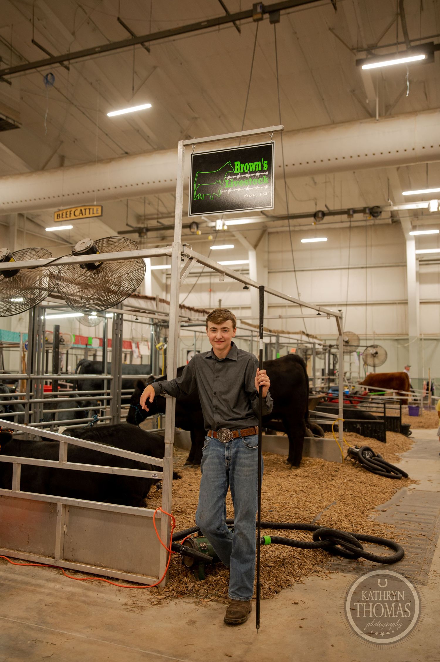 Inside a livestock barn, someone poses near metal gates with digital displays visible overhead.