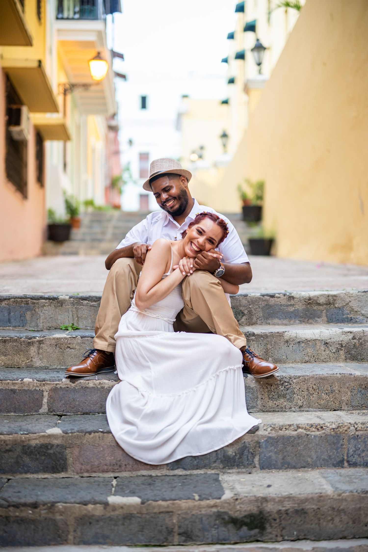 A couple poses playfully on stone steps between colorful buildings.